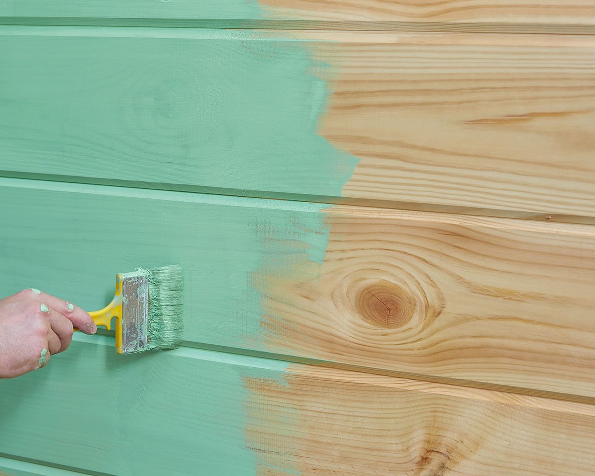 hand paints wooden vertical surface with green paint